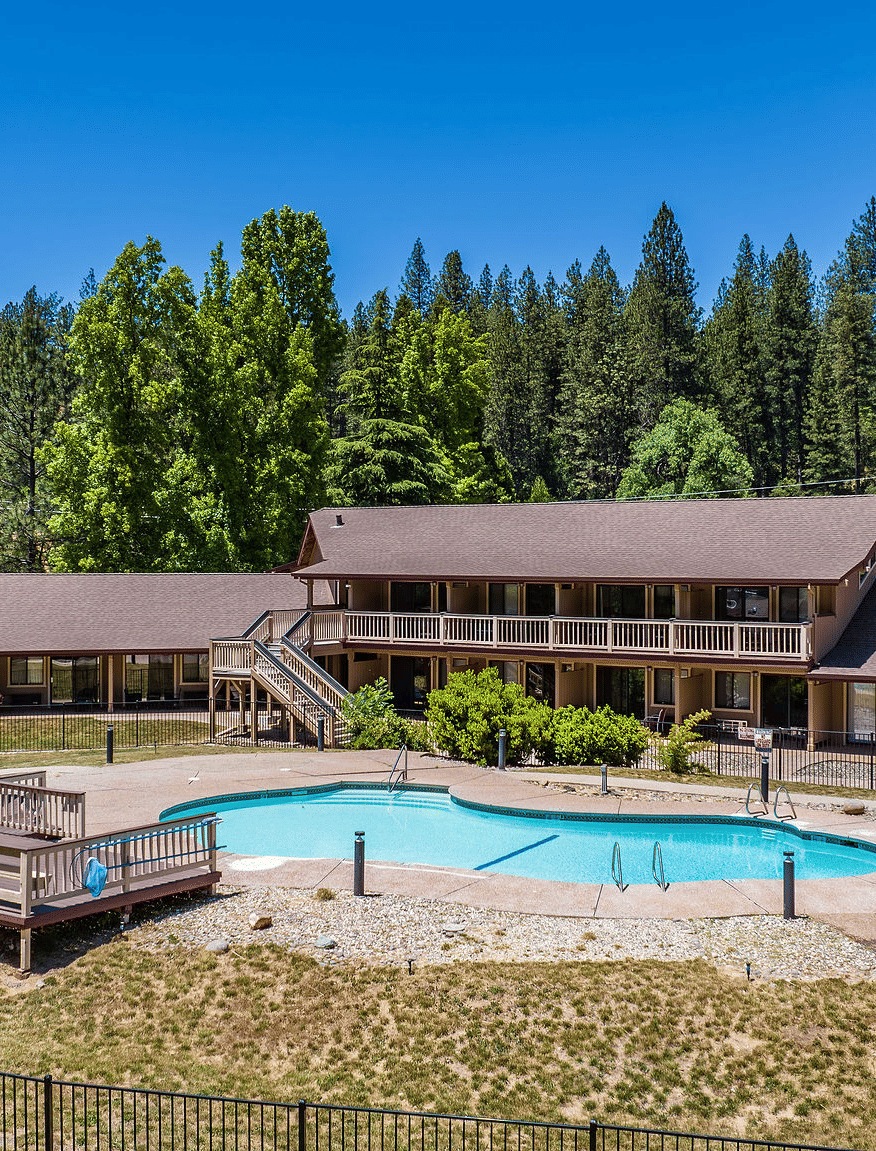 An aerial or elevated view of a multistory hotel complex nestled in a forest, featuring an outdoor swimming pool and sun deck - Amador Hotel