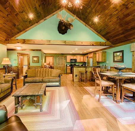 full view image of the living area with a seating area and a dining table along with a decorative stag head hanging above the room - Historic Tapoco Lodge