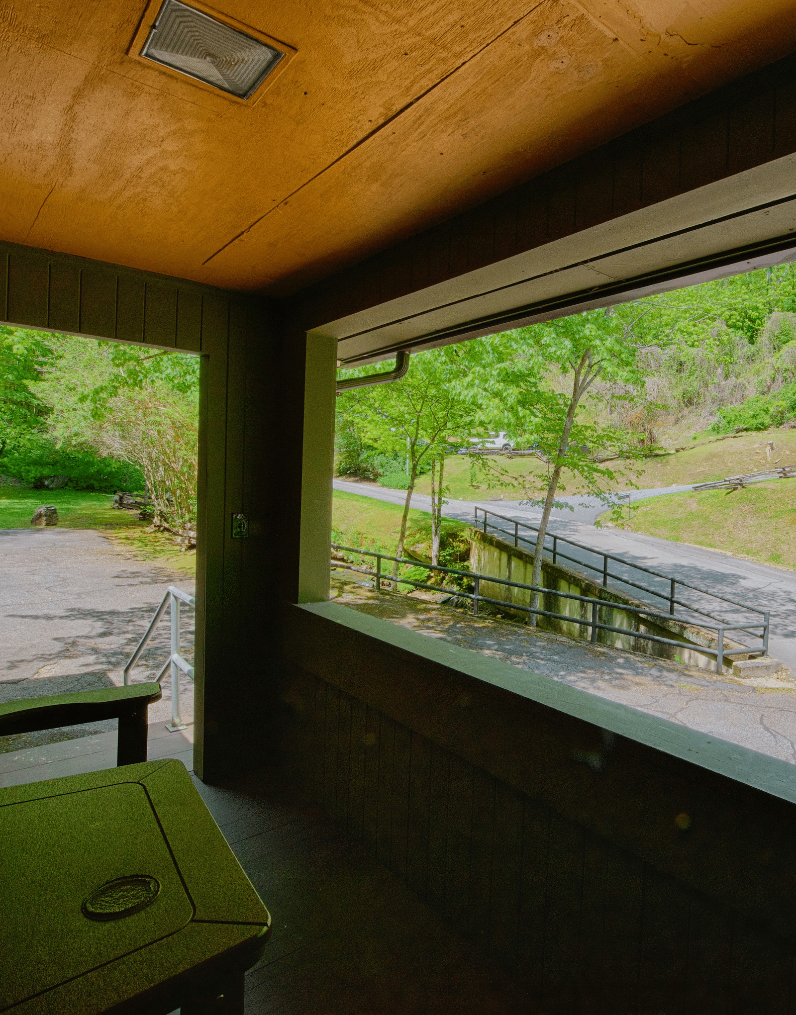 an indoor porch with a wooden armchair facing towards the pathway outside the cabin - Historic Tapoco Lodge