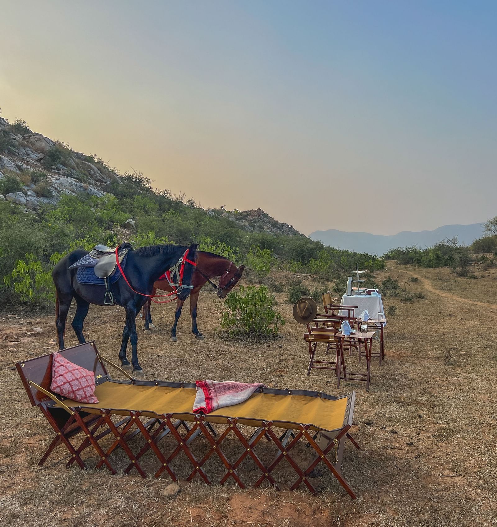 An image of two horses near a seating arrangement with mountains in the background - Utsav Camp Sariska