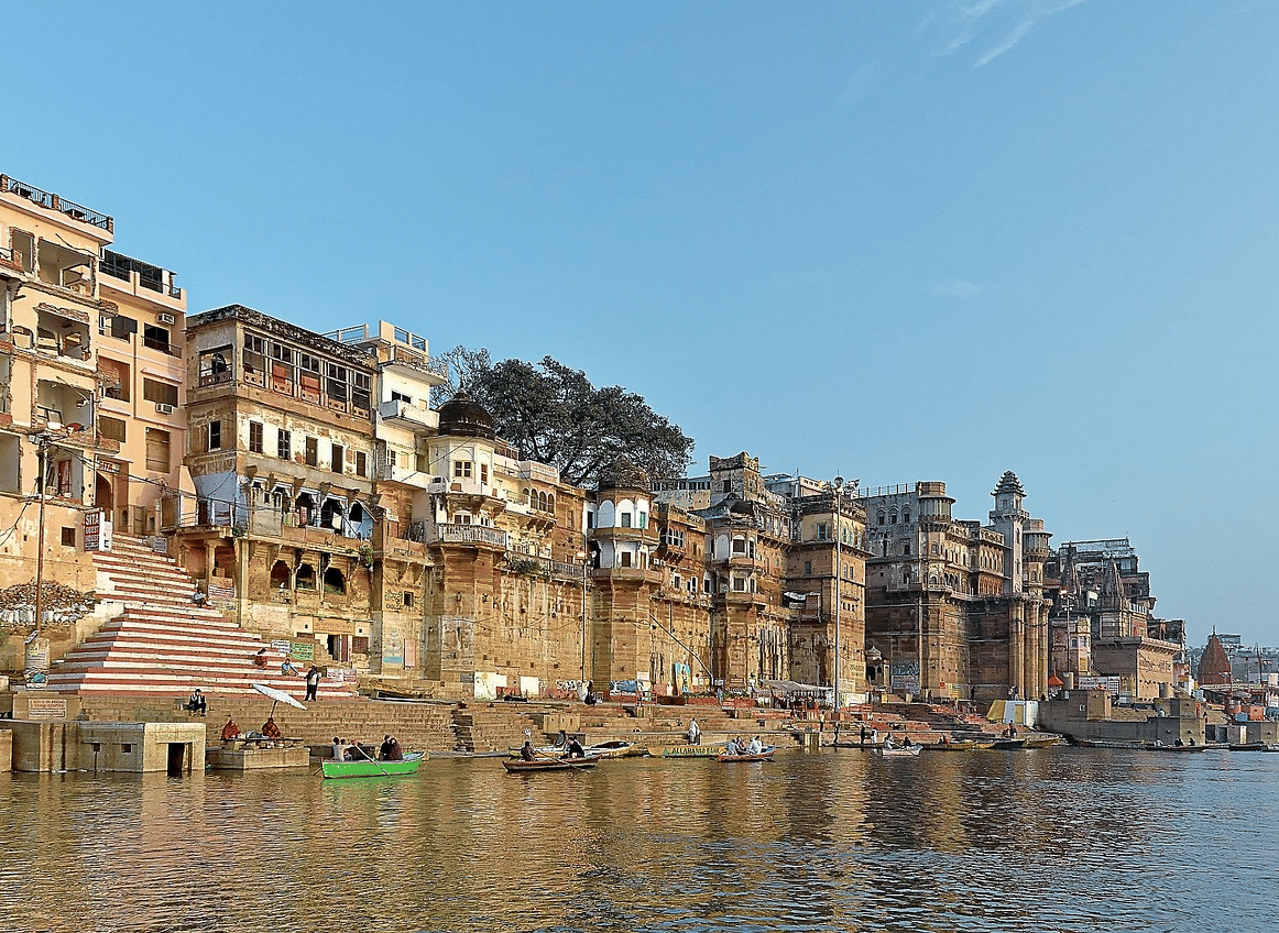 A riverfront view of a town with multi-storey buildings lining the banks of the river under a clear blue sky