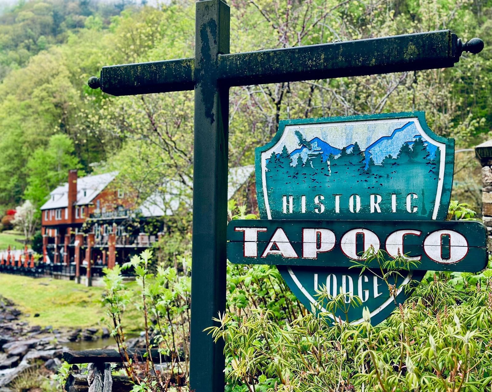 A close-up shot of a signboard reading 'Historic Tapoco lodge' with the exterior of the hotel in the background surrounded by greenery.
