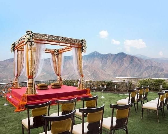 a mandap set up meant for wedding ceremony on manicured lawn with chairs facing it and in the background there are hils at a distance- neer ganga Resorts