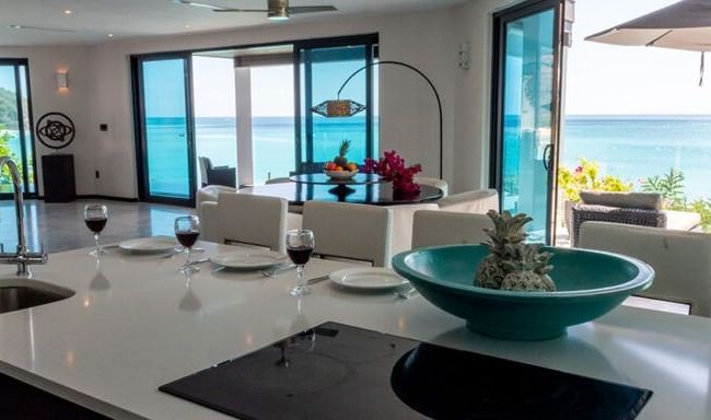 A stylish open-plan kitchen and dining space with ocean views, tropical decor, and glasses of wine set for a relaxed seaside meal - Tamarind Hills Resort and Villas - Antigua