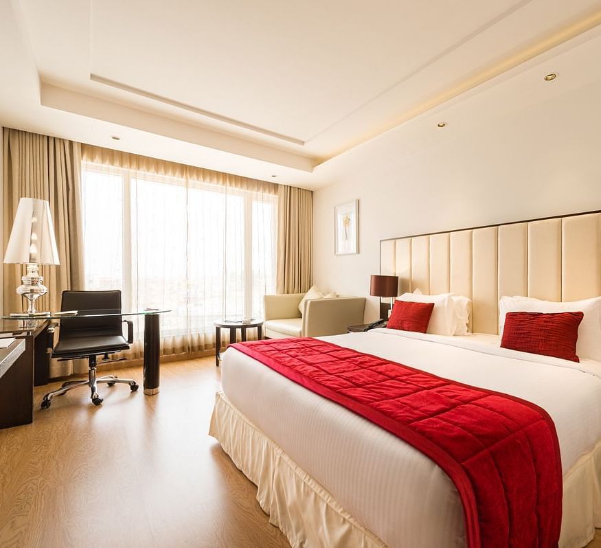 A well-lit hotel room with two twin beds covered in red bedspreads and white sheets - TGI Grand Fortuna, Hosur