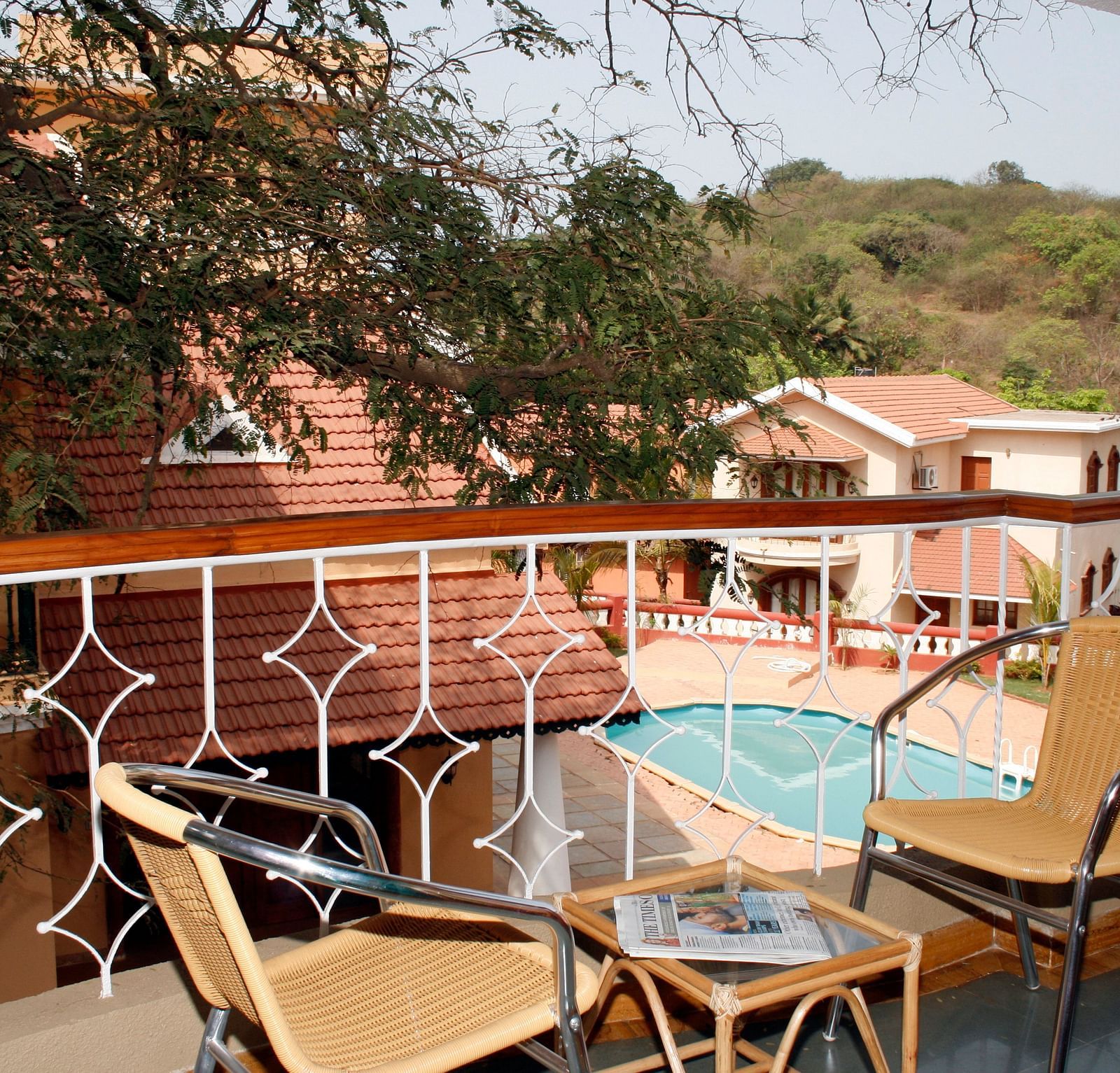 two chairs and a coffee table on the balcony with a view of the greenery in distance and the pool inside the premises