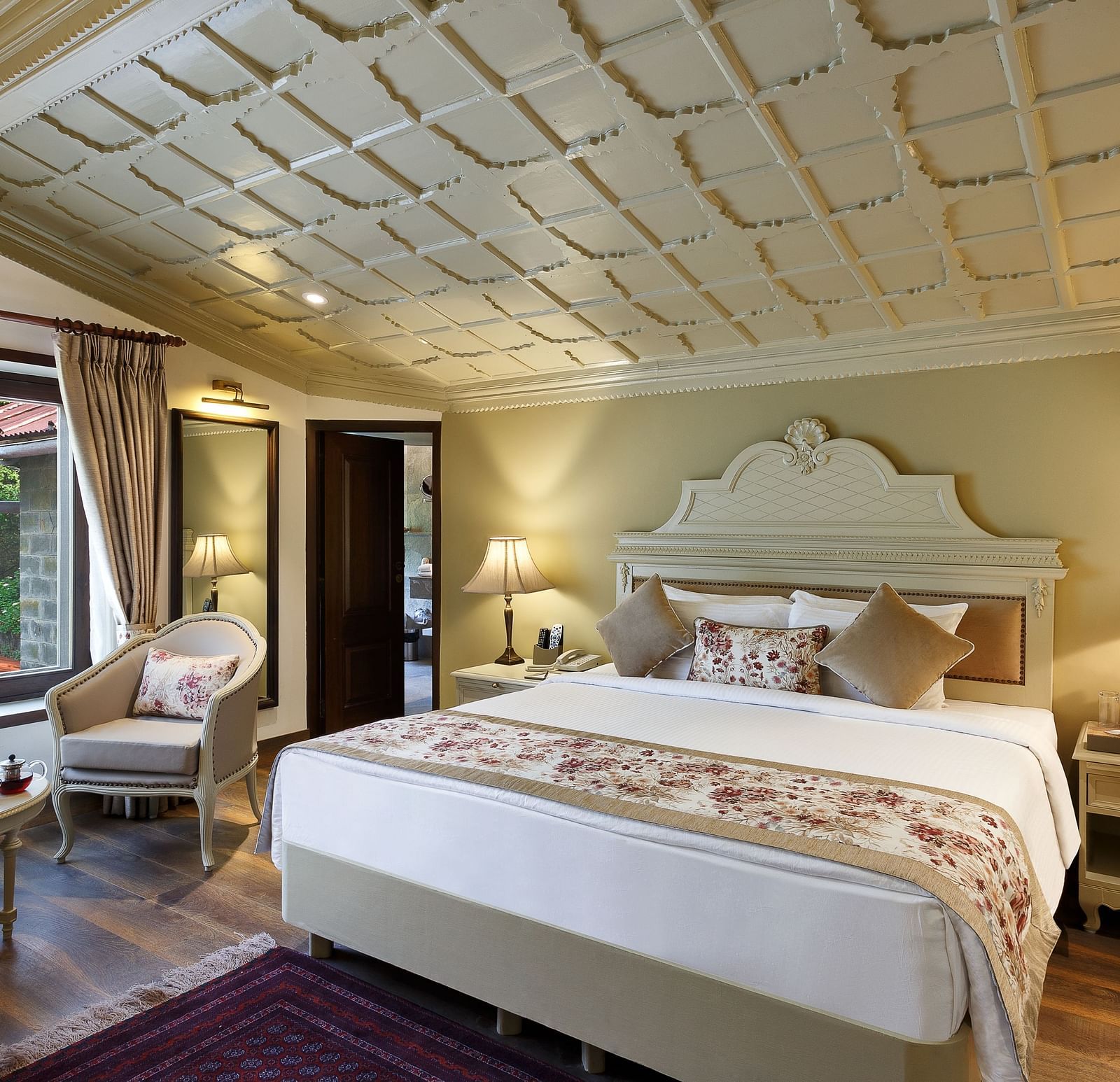 A full view of a room with a royal bed, chair, table and a huge glass window - the naini retreat, nainital.