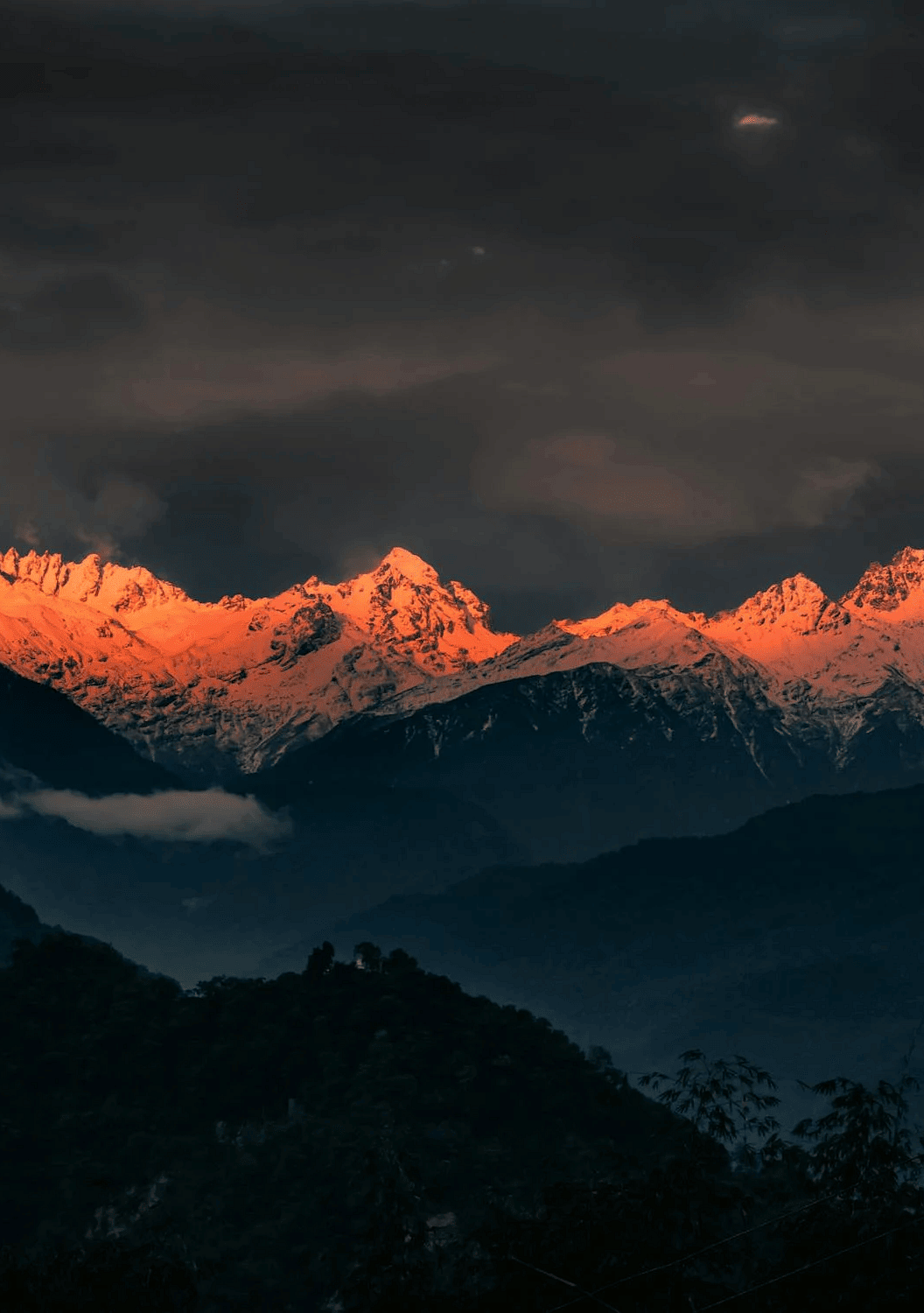 Image of a snow clad mountain with the rays of the sun shining on the tip of the mountain.