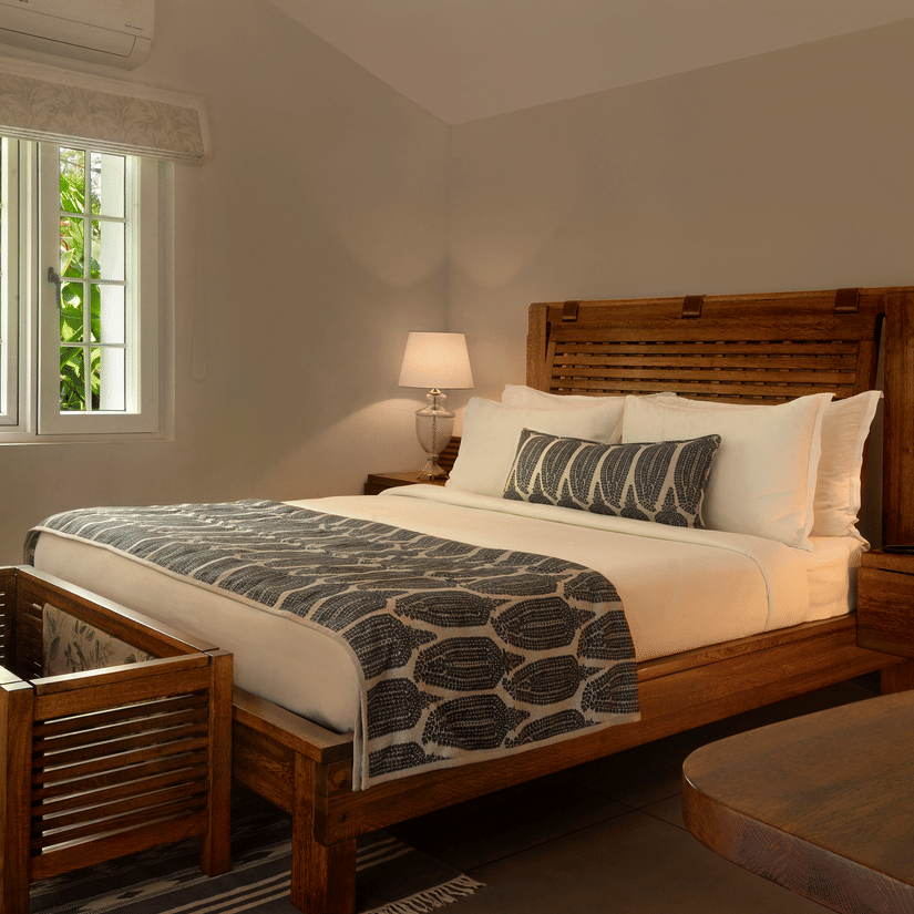 Elegant bedroom with a large bed, two lamps, and a window with greenery outside at Amanvana Spa Resort, Coorg - Luxury Resort