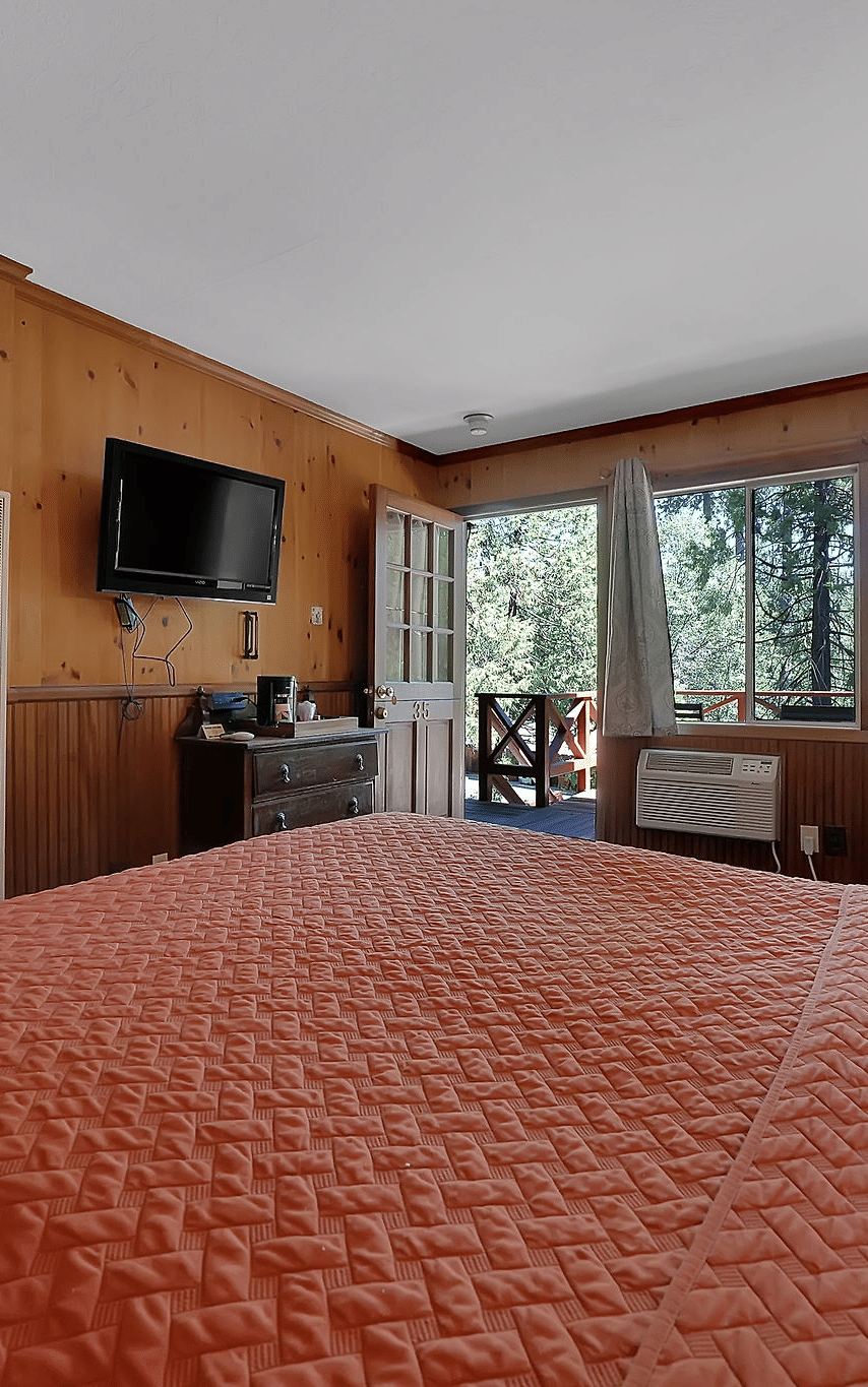 A view of a room at Narrow Gauge Inn with a double bed and sliding doors opening to a balcony.