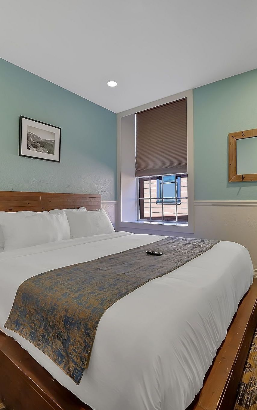 A comfortable room at The Groveland Hotel with sage green walls, wooden bed, blue patterned runner, TV, and convenient coffee station.