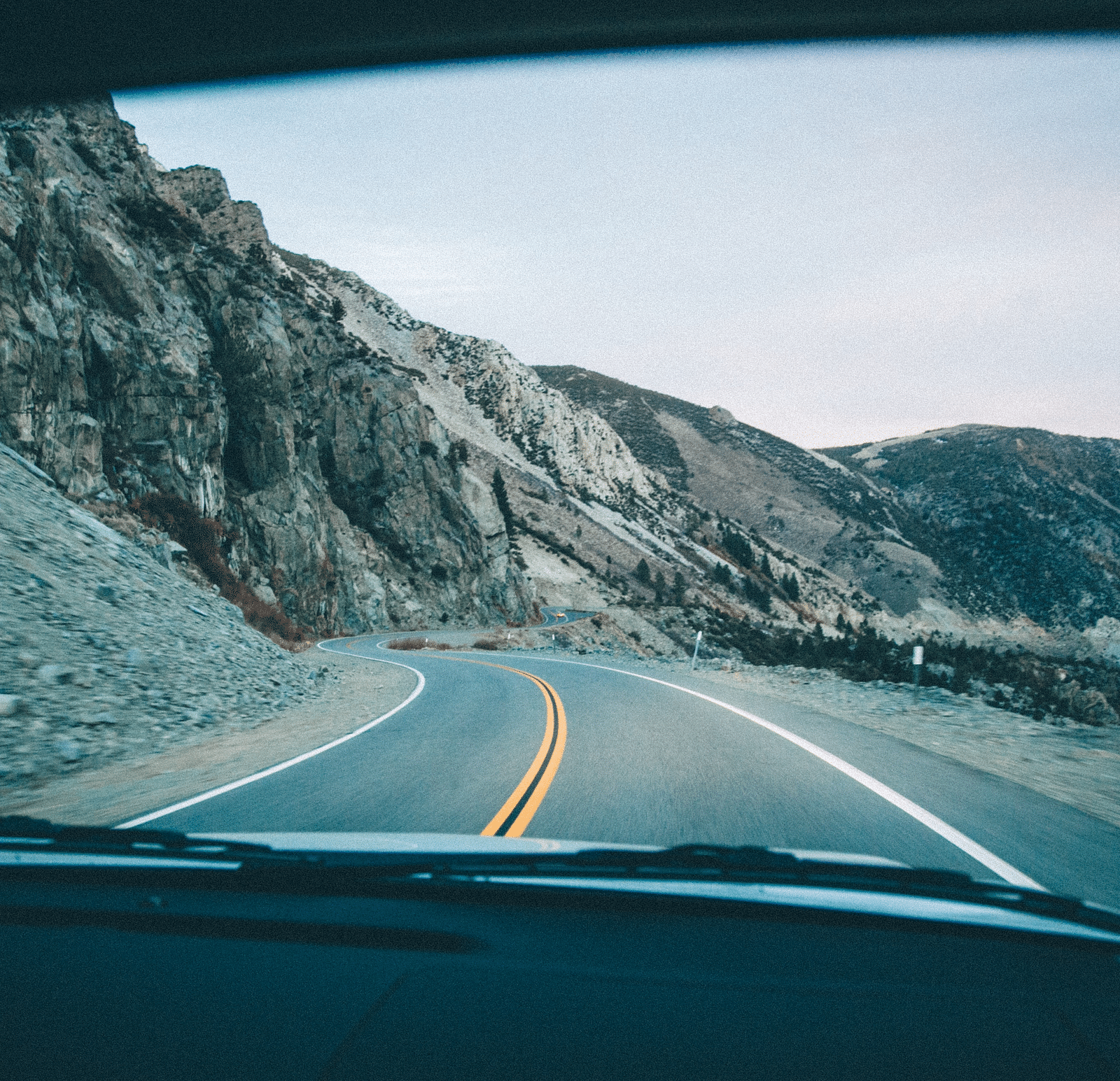 an image captured inside of a vehicle, featuring the road ahead surrounded with the mountain range followed.