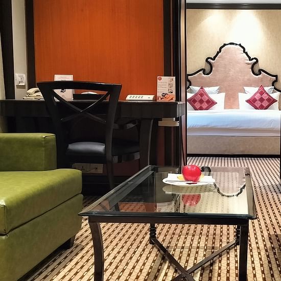 Hotel room with twin chairs, a coffee table, and a bed framed by lamps and wall art.