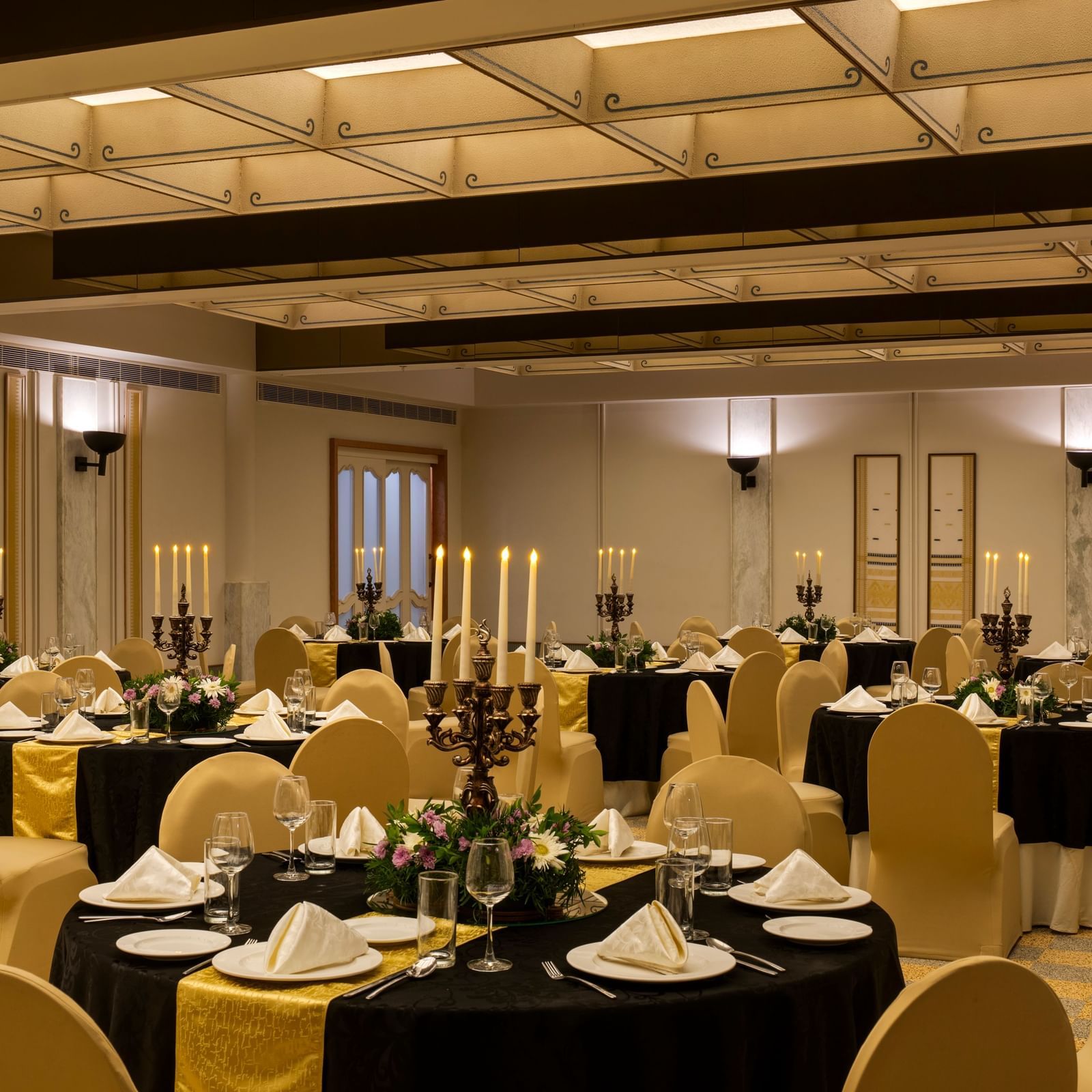  A well-appointed banquet room at Shilton International, Kochi with round tables adorned with settings and candelabras.
