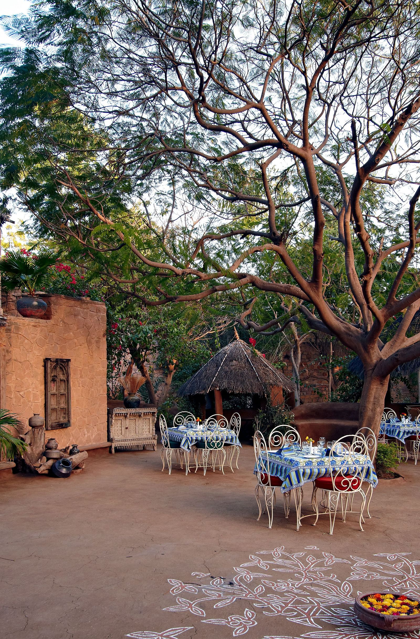 An image of the outdoor seating arrangement of the Taasli Restaurant at Manvar Shergarh with greenery around - Manvar Resort & Desert Camp