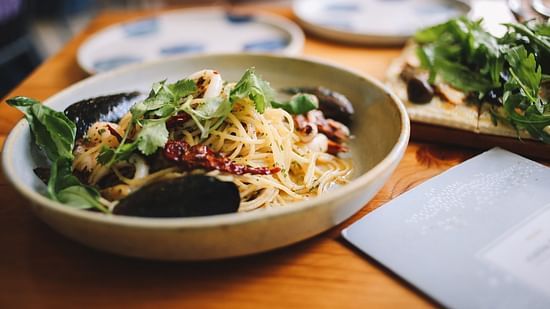an image of a bowl with noodles garnished with red dried chillies and coriander leaves 