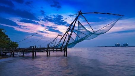 Chinese fishing nets extending into the sea under a blue evening sky in Fort Kochi.