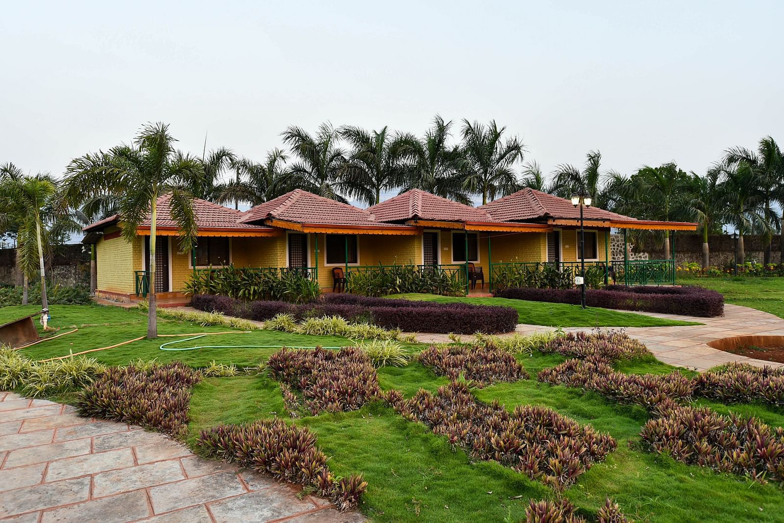 Facade of Deluxe Cottage at the Kanila Resort featuring a lush green lawn with a pathway and trees. 