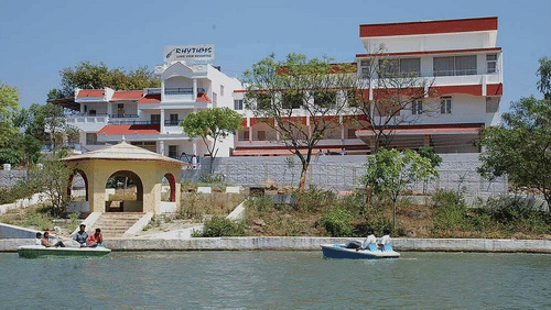 Lakeside resort with red and white buildings and guests boating nearby.