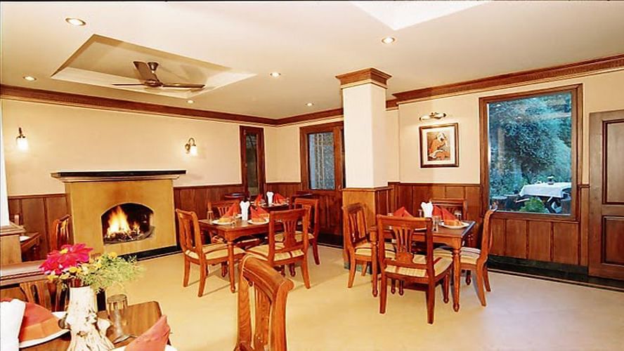 A room with tables with chairs arranged in clusters and a fireplace on one side of the room - Sun N Snow Inn, Kausani