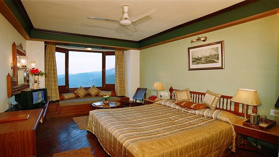 A wide view of a bedroom with a large bed and two side lamps on each side of the bed, a desk and a curved sofa - Sun N Snow Inn, Kausani