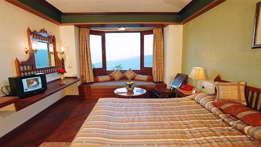 A bedroom with a large bed opposite a desk fixed on the wall and a curved sofa in front of the window - Sun N Snow Inn, Kausani