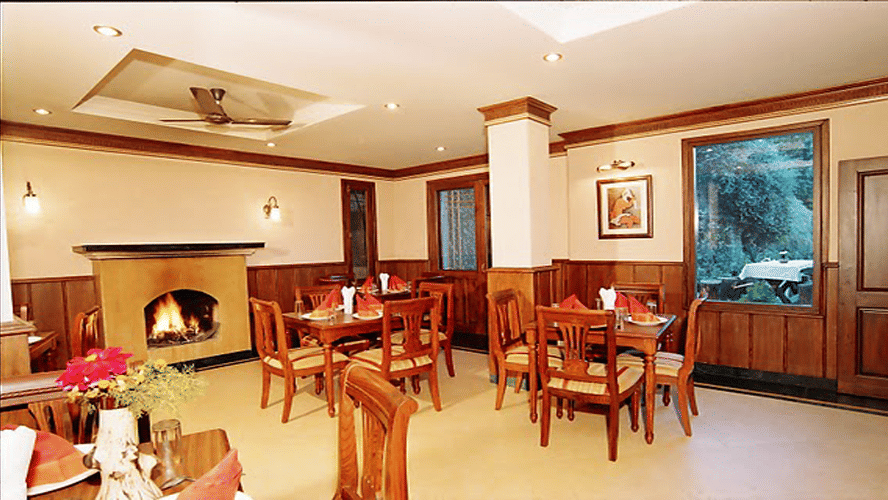 A room with tables with chairs arranged in clusters and a fireplace on one side of the room - Sun N Snow Inn, Kausani