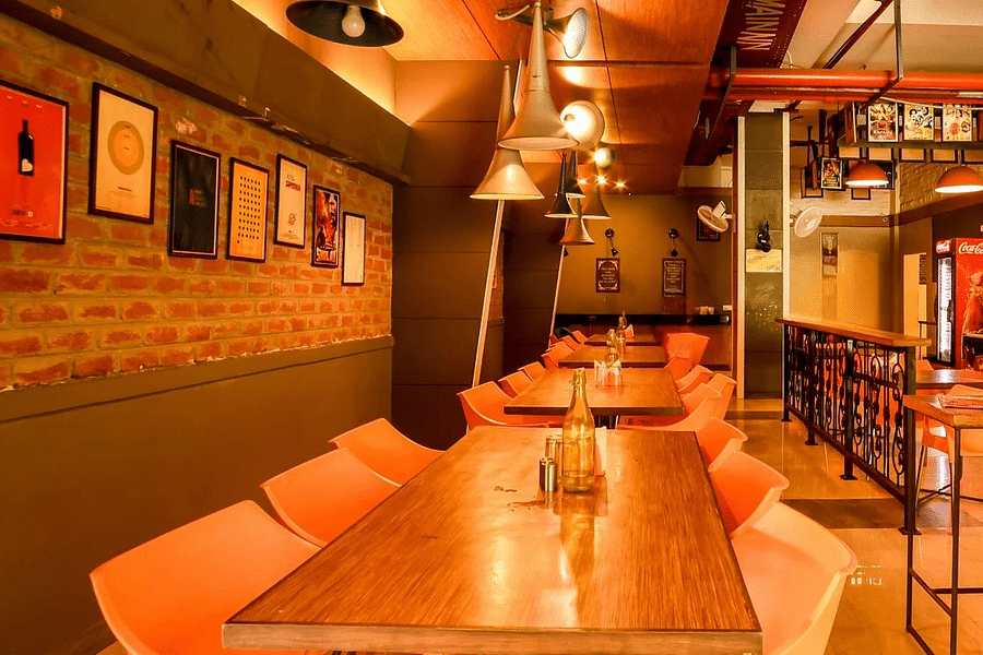 alt-text An image of a restaurant with several chairs and tables, ceiling lights hanging, photo frames on the walls, and other things - Max Hotel Jabalpur