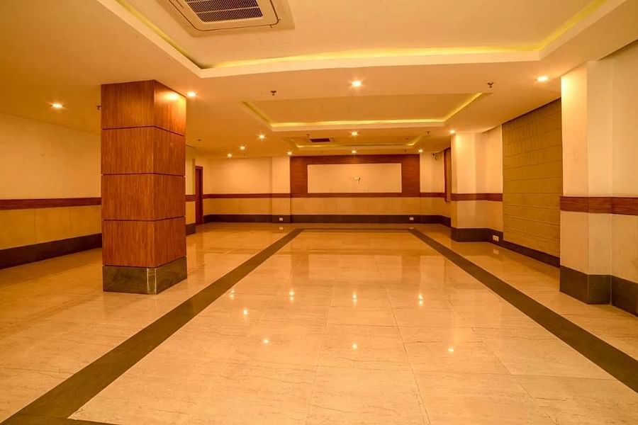 alt-text A spacious banquet hall with polished marble flooring, wooden pillars, and a minimalistic design featuring a large open space and a stage at the end.