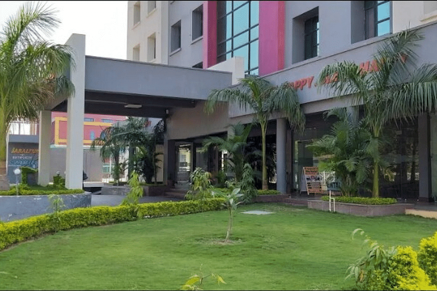 alt-text The front view of a modern hotel with a colorful facade, surrounded by a landscaped lawn and palm trees, under a blue sky with fluffy clouds.