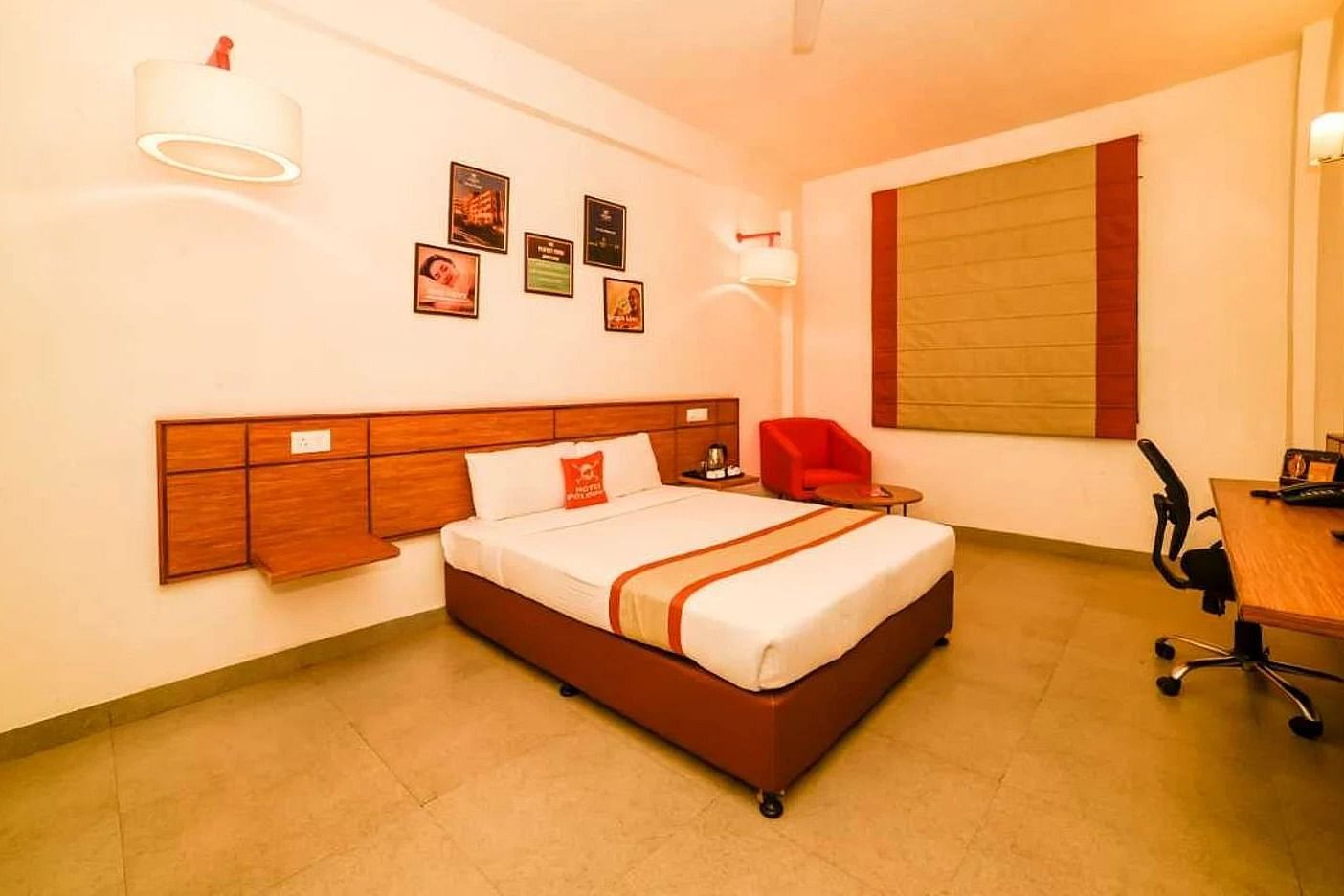 A bedroom at Max Hotel Prayagraj, featuring a bed with white linens and a striped bed runner, a wooden headboard, and a desk with a chair.