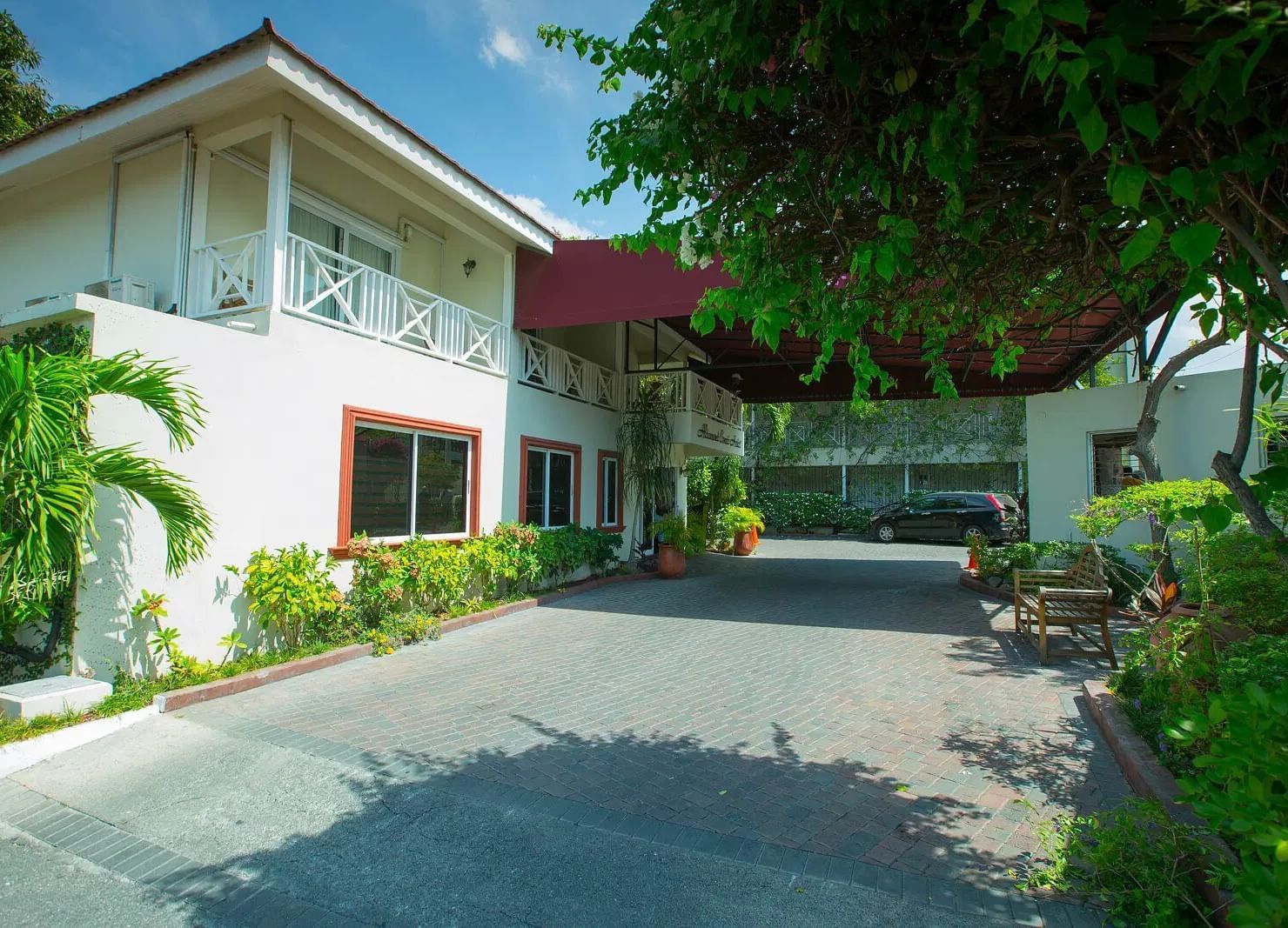 A white house with a roof is seen from a paved driveway leading up to its entrance | Altamont Court, Jamaica