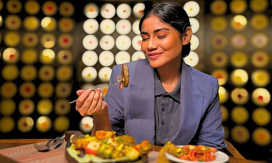 A woman dressed professionally, enjoying BBQ at a restaurant, with a plate of grilled food in front of her.