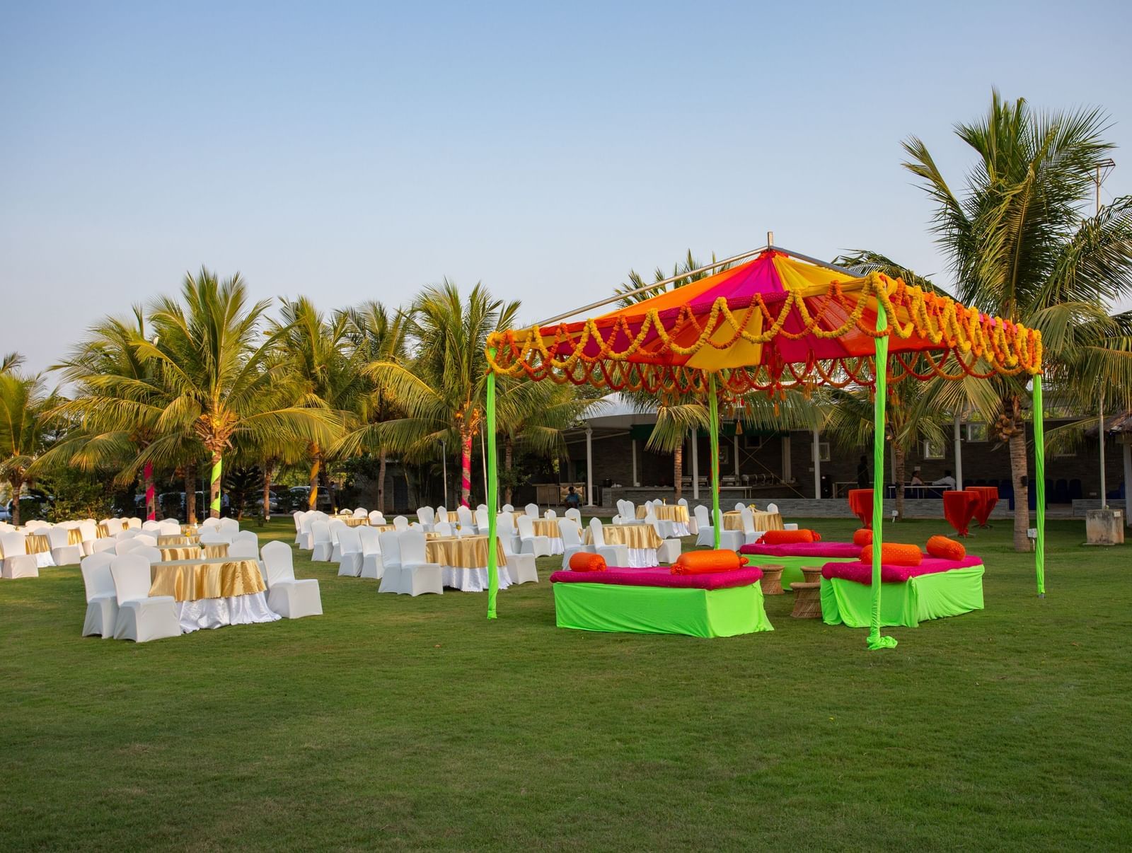An outdoor event setup with an orange and yellow tent, green and red seating, and numerous white chairs on a grassy lawn | Grande Pavillion | Grand Bay Resort and Spa