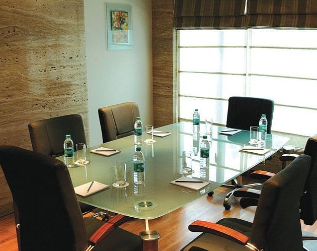 Image of a meeting room at our hotel featuring a glass table with seven chairs around it. | Mirage Hotel