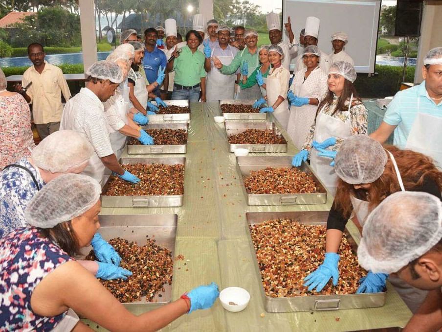 People mixing dry fruits in trays for cake preparation.