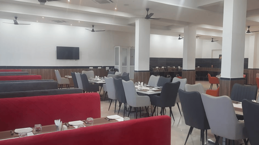 A brightly lit dining area features tables with red bench seating and grey chairs - Kankidham Lords Inn