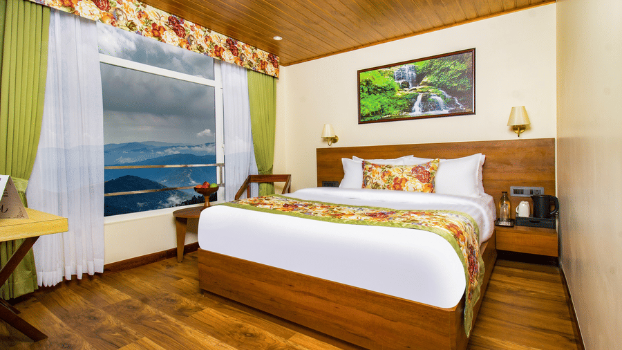 Deluxe Room featuring wooden interiors, king size bed, large window with views of hills, and cosy seating making it one of the best places to stay in Darjeeling | Mount Lungta Boutique Hotel & Spa