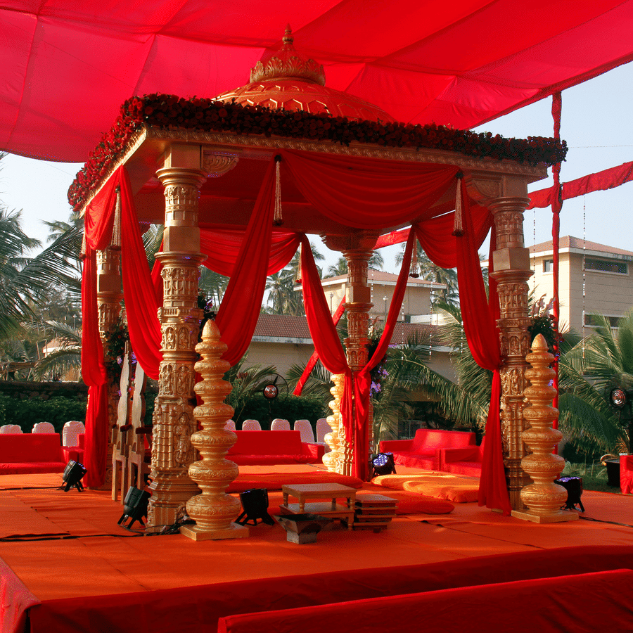 A ceremonial pavilion with decorative draping and pillars set up outdoors with palm trees in the background.
