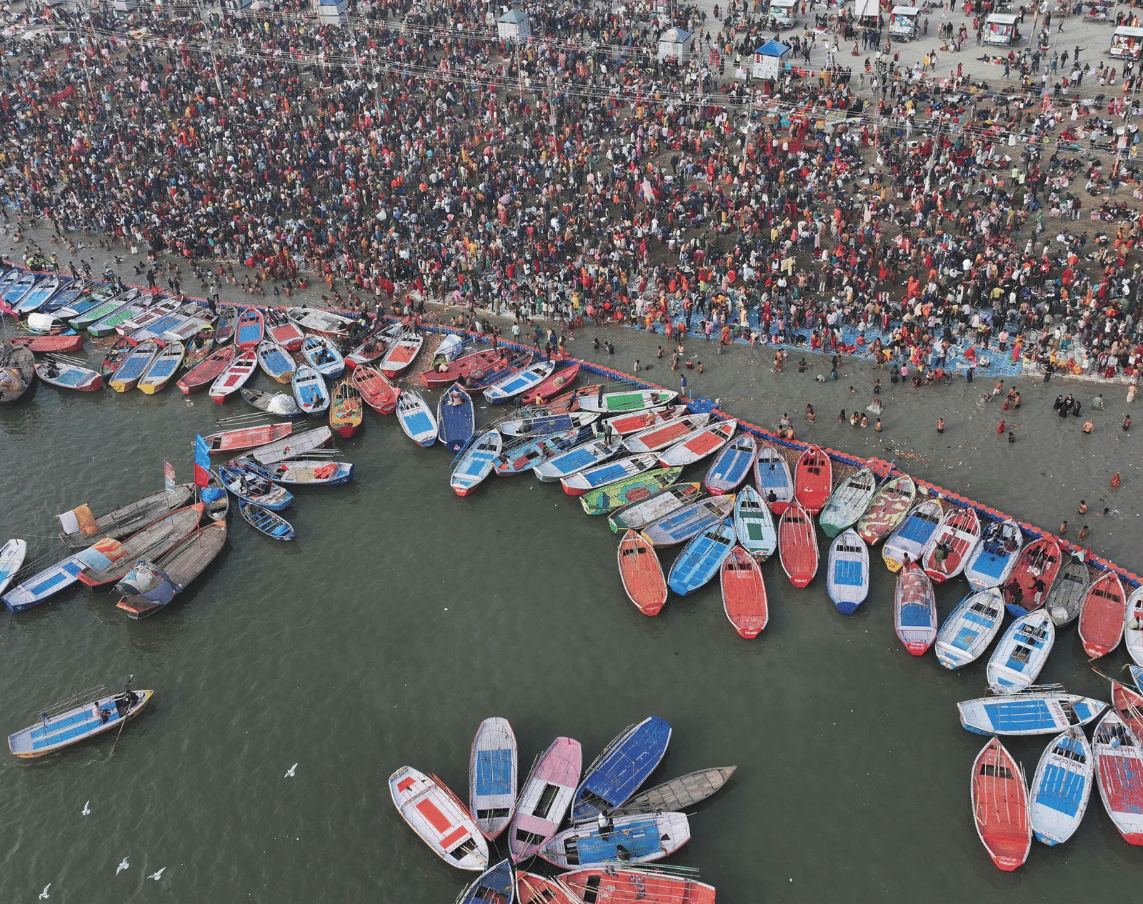 Aerial view of Triveni Ghat with boats parked on the shore and crowd near the edge.