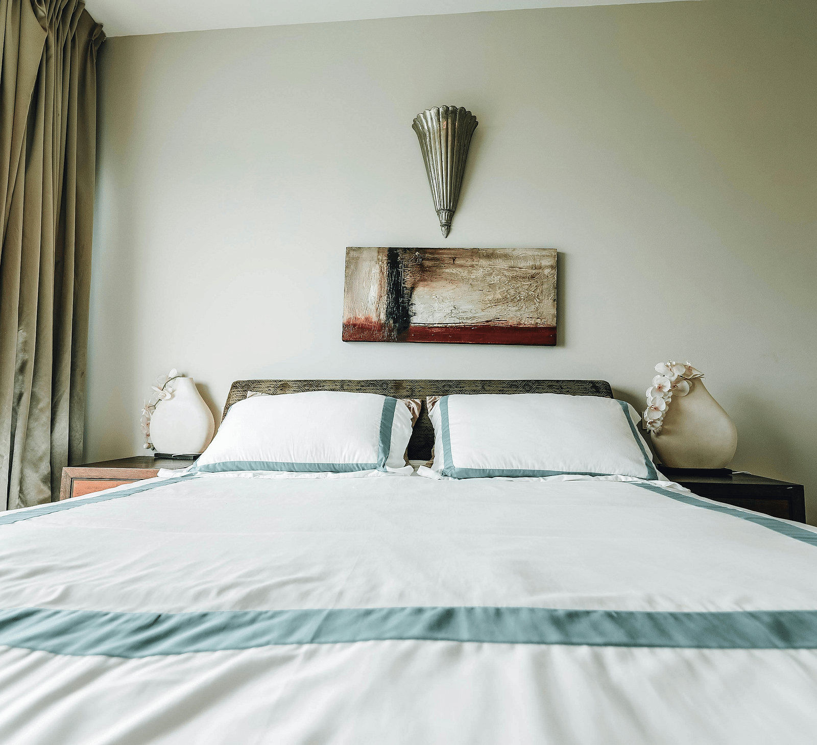 An image of a room featuring a bed, bed side tables, and a painting hung on the wall
