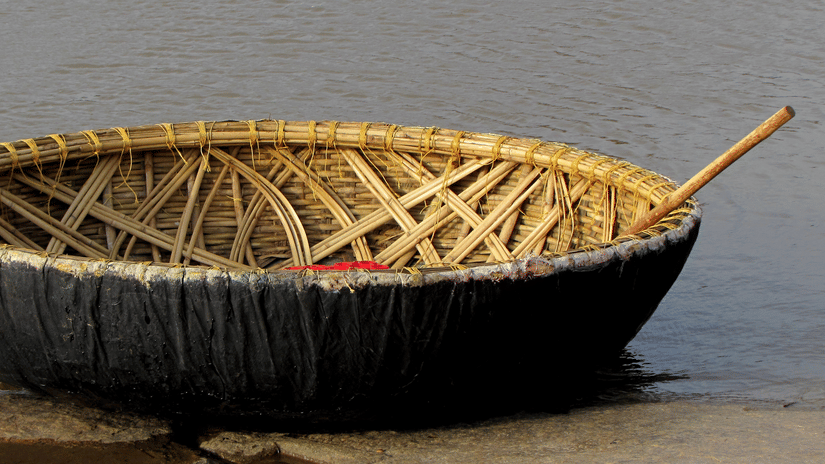 A close up of a Coracle boat with an oar kept inside it, floating on a waterbody near a step. These coracle rides provide opportunities to visit the many places to see in Kabini.