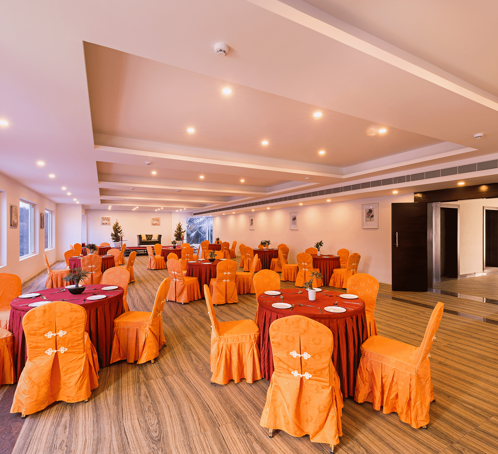 Spacious dining hall with orange chair covers and round tables set for a meal - TGI Grand Fortuna, Hosur