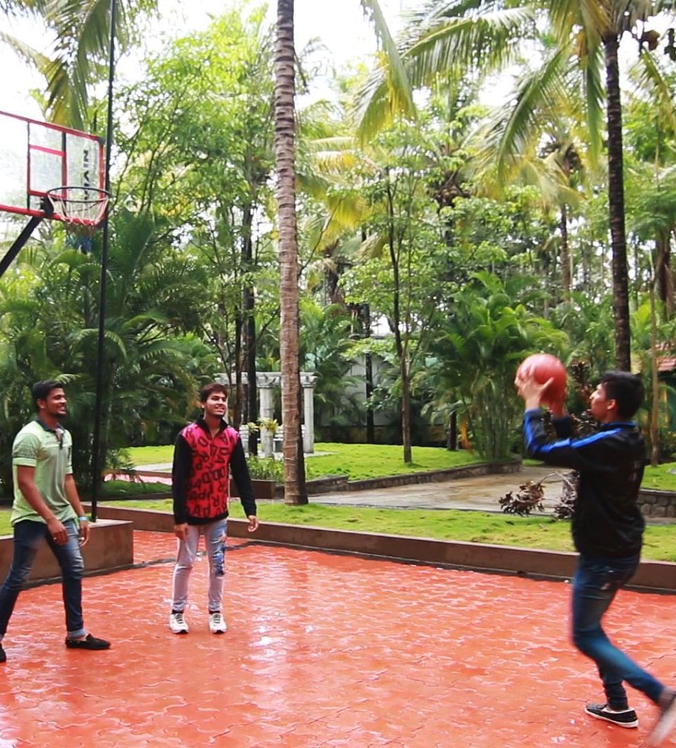Image of four people playing basketball with trees in the background at Parampara Resort & Spa, Kushalnagar.