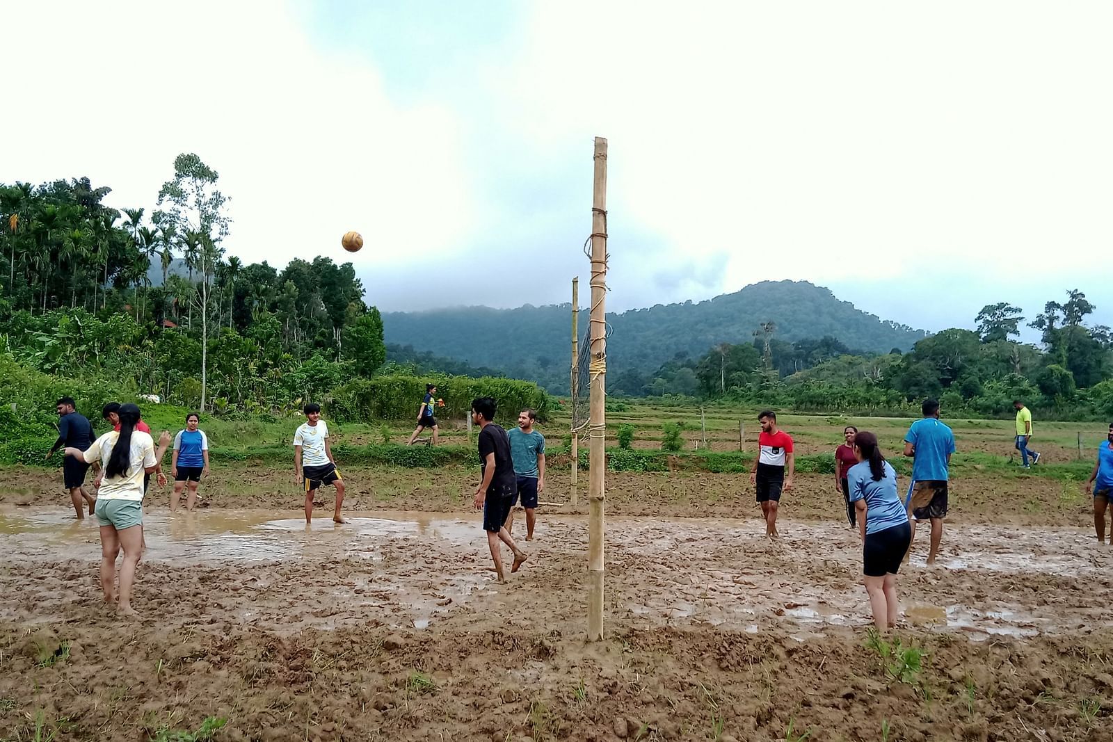 Group playing volleyball in a muddy field with a scenic mountain backdrop - Evergreen County