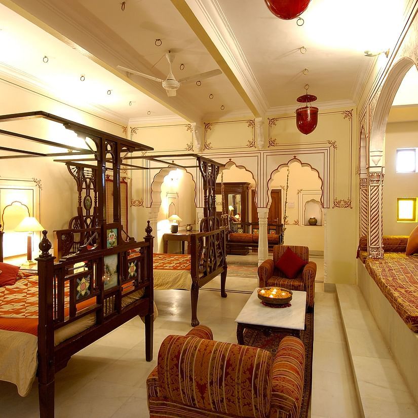 a brightly lit room with a two large beds with a canopy and sofas for sitting - Hotel Castle Mandawa, Jhunjunu