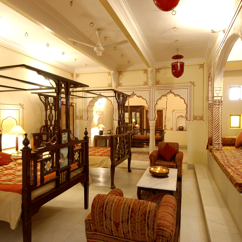 A brightly lit Suite room with a two large beds with a canopy and sofas for sitting at Hotel Castle Mandawa, Jhunjunu