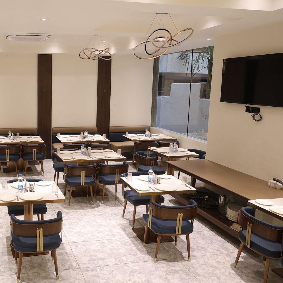 A brightly lit dining area at Lords Eco inn Jamnagar Maheshwari Nagar with multiple tables chairs and stylish lighting.