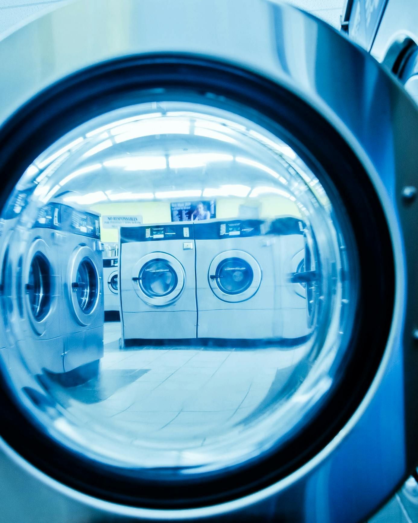 A close-up view through a washing machine door, showcasing modern laundry facilities in a clean, well-lit space.