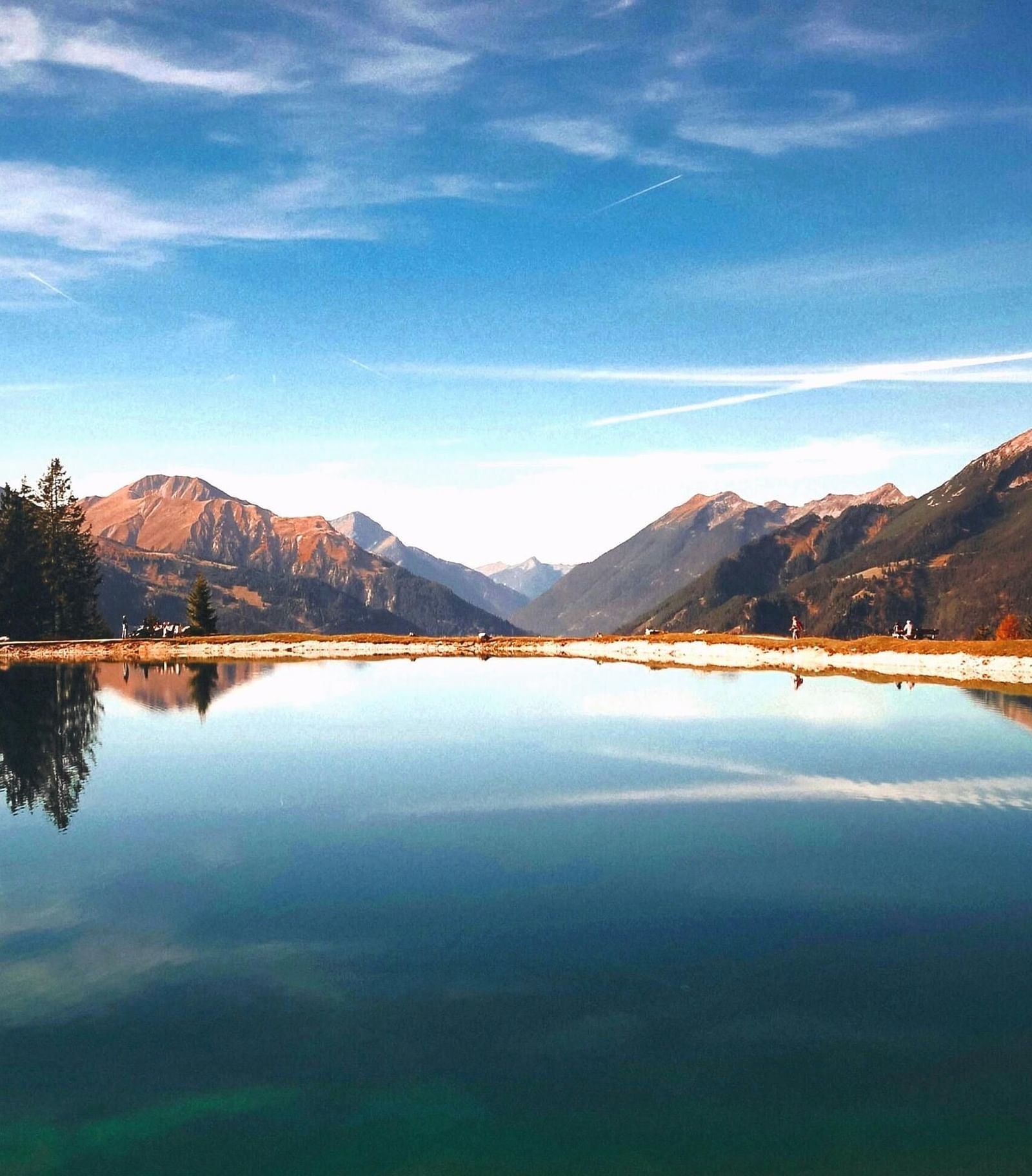 A serene mountain landscape featuring a reflective lake surrounded by towering peaks and lush trees.
